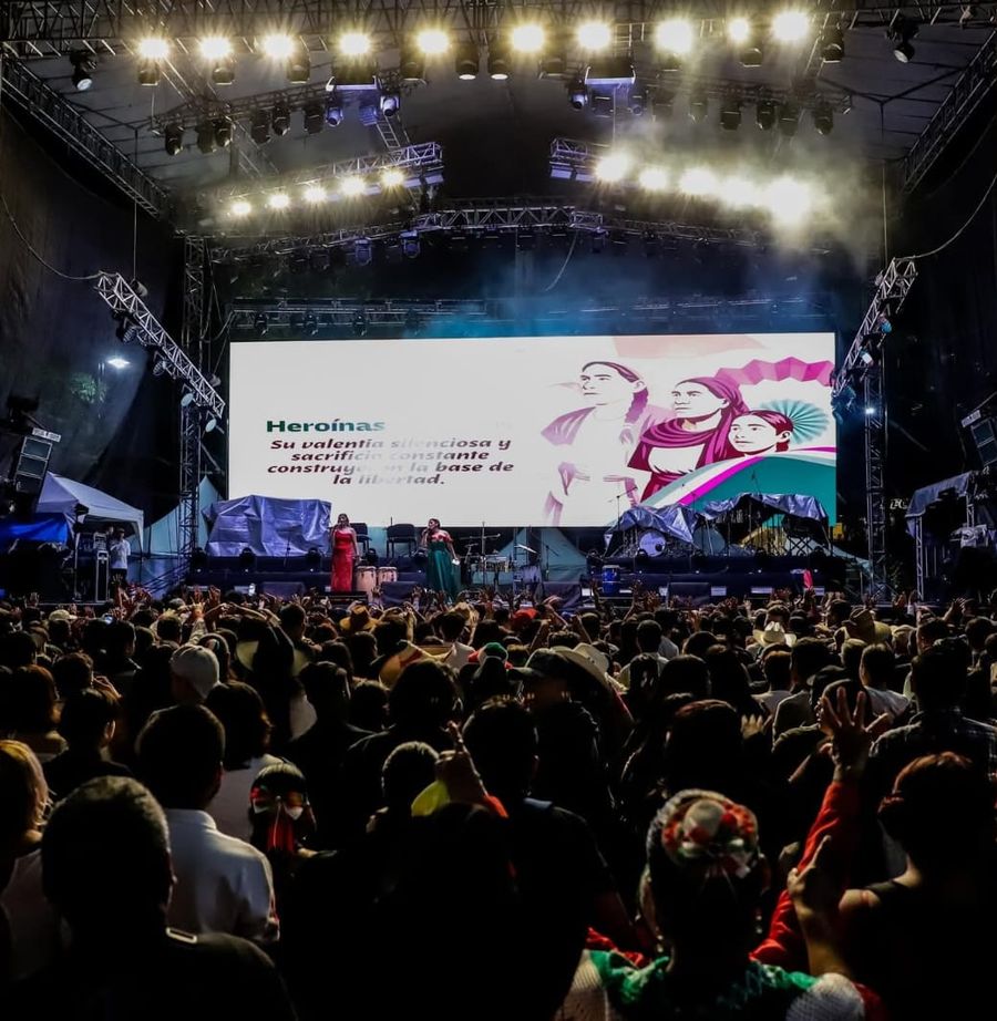 Escenario con pantalla LED e iluminación frente a miles de asistentes en un evento público nocturno