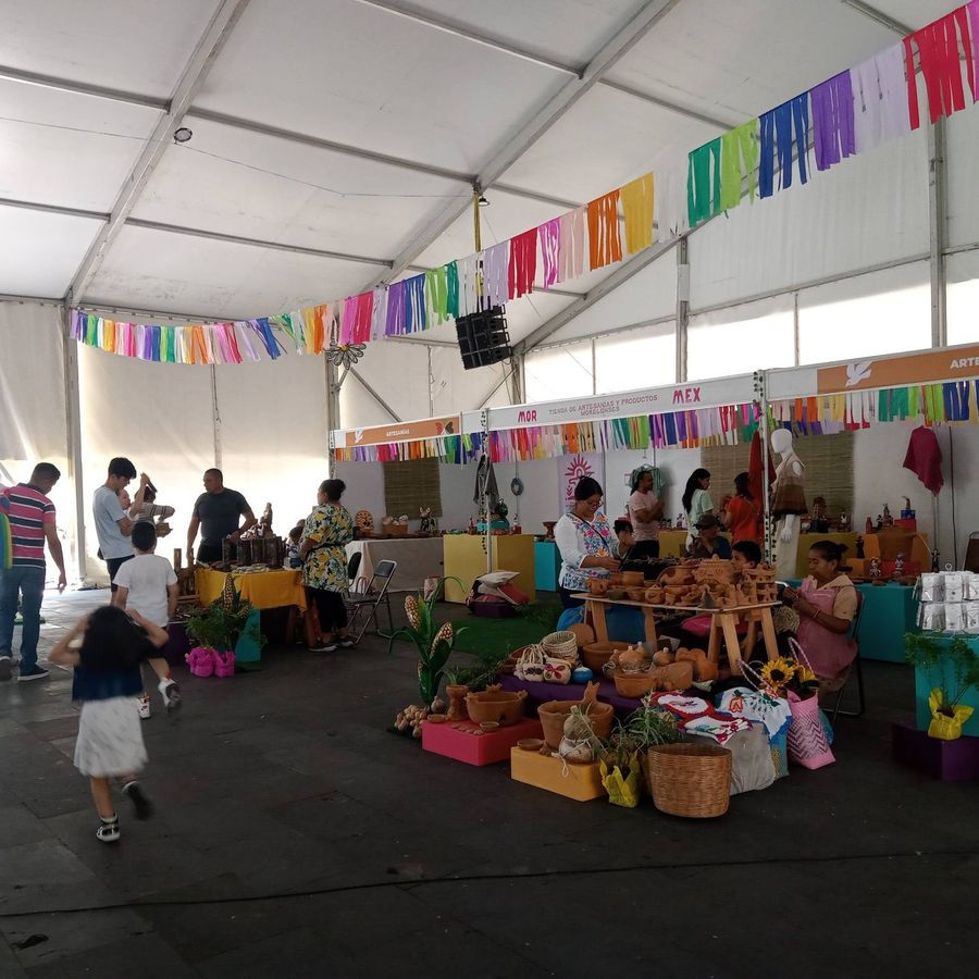 Feria bajo carpa con puestos de artesanías y papel picado