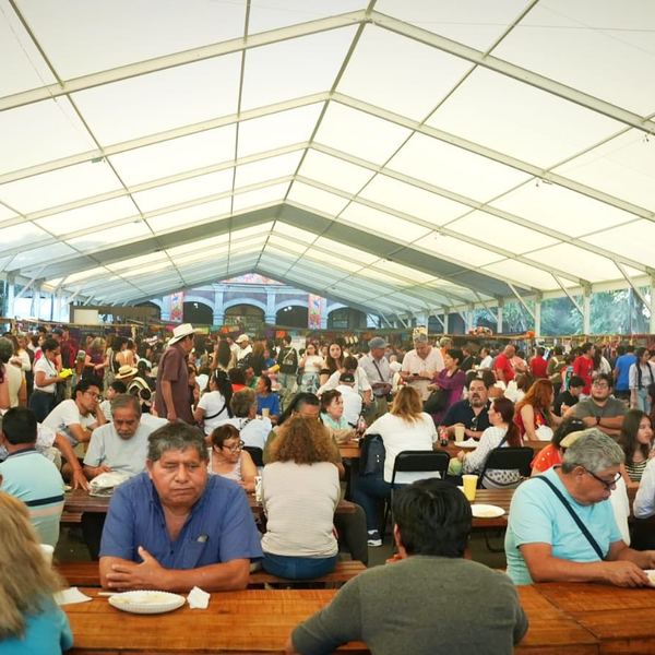 Comensales en mesas largas bajo una carpa en un foro gastronómico
