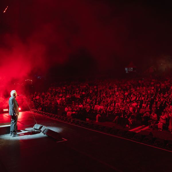 Escenario iluminado de rojo frente a miles de asistentes en un concierto al aire libre
