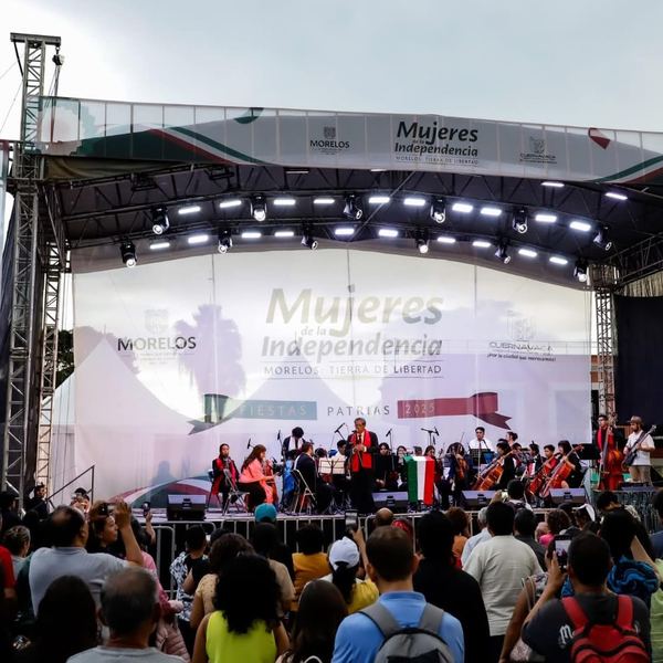 Escenario con techo y lona impresa de Fiestas Patrias en una plaza pública llena de asistentes