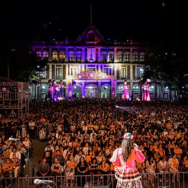 Miles de asistentes en un evento público nocturno frente a un edificio histórico iluminado