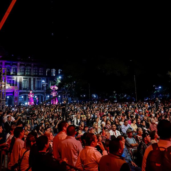Público en un evento nocturno frente a un edificio histórico iluminado de morado