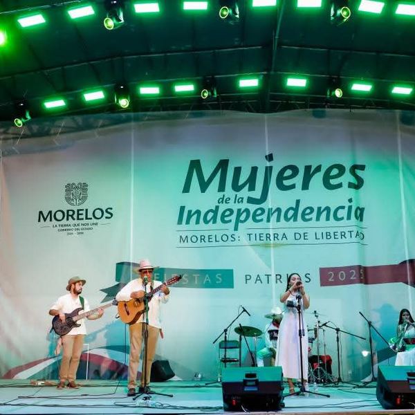 Músicos en el escenario de Fiestas Patrias con iluminación verde y lona del Gobierno de Morelos